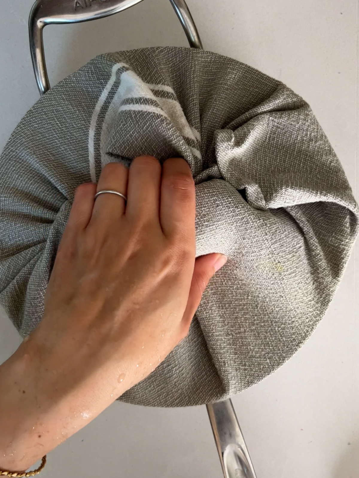 A hand holding the lid of a pot wrapped in a grey tea towel.