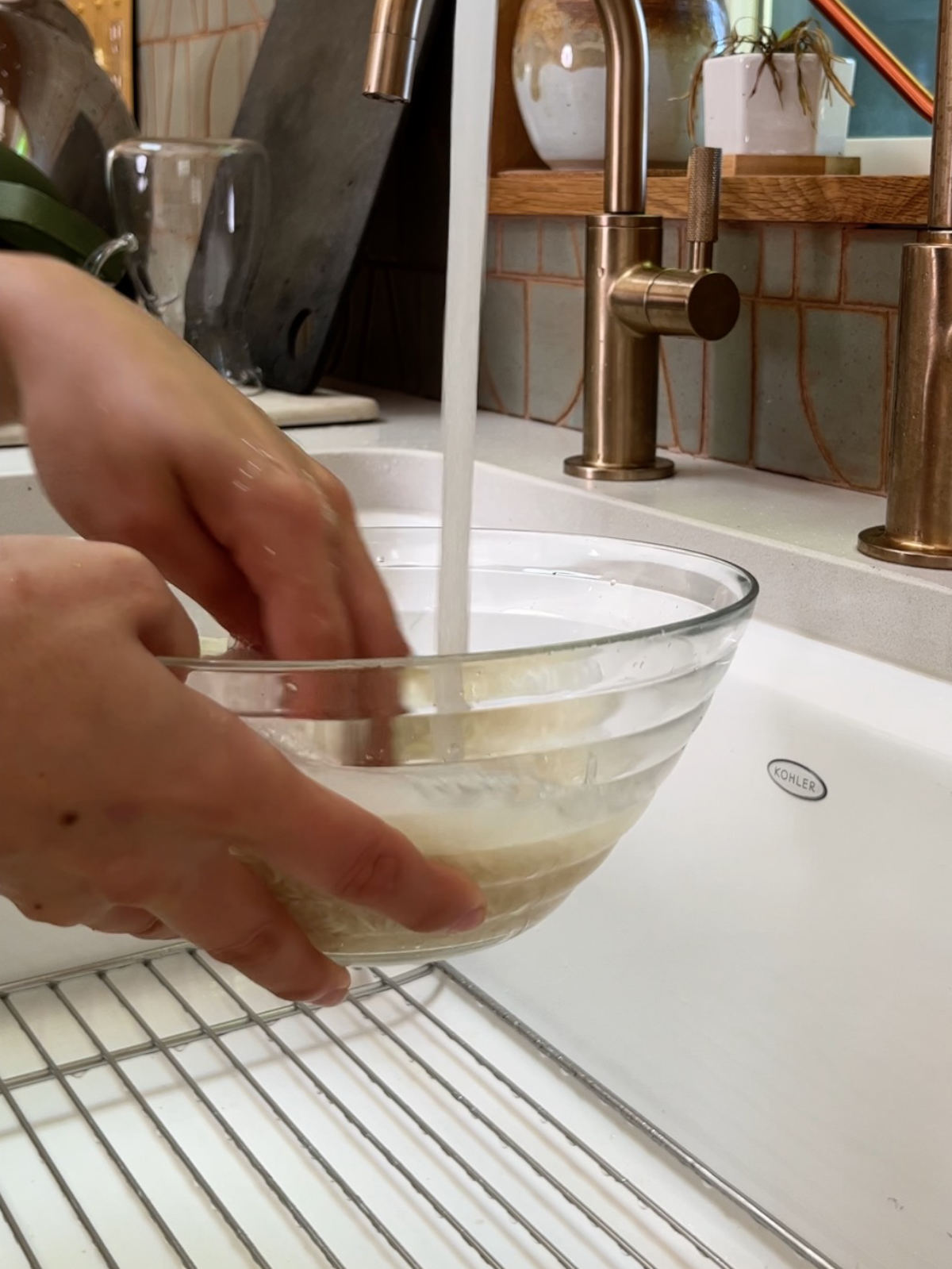 Two hands washing rice in a glass bowl in a white sink.