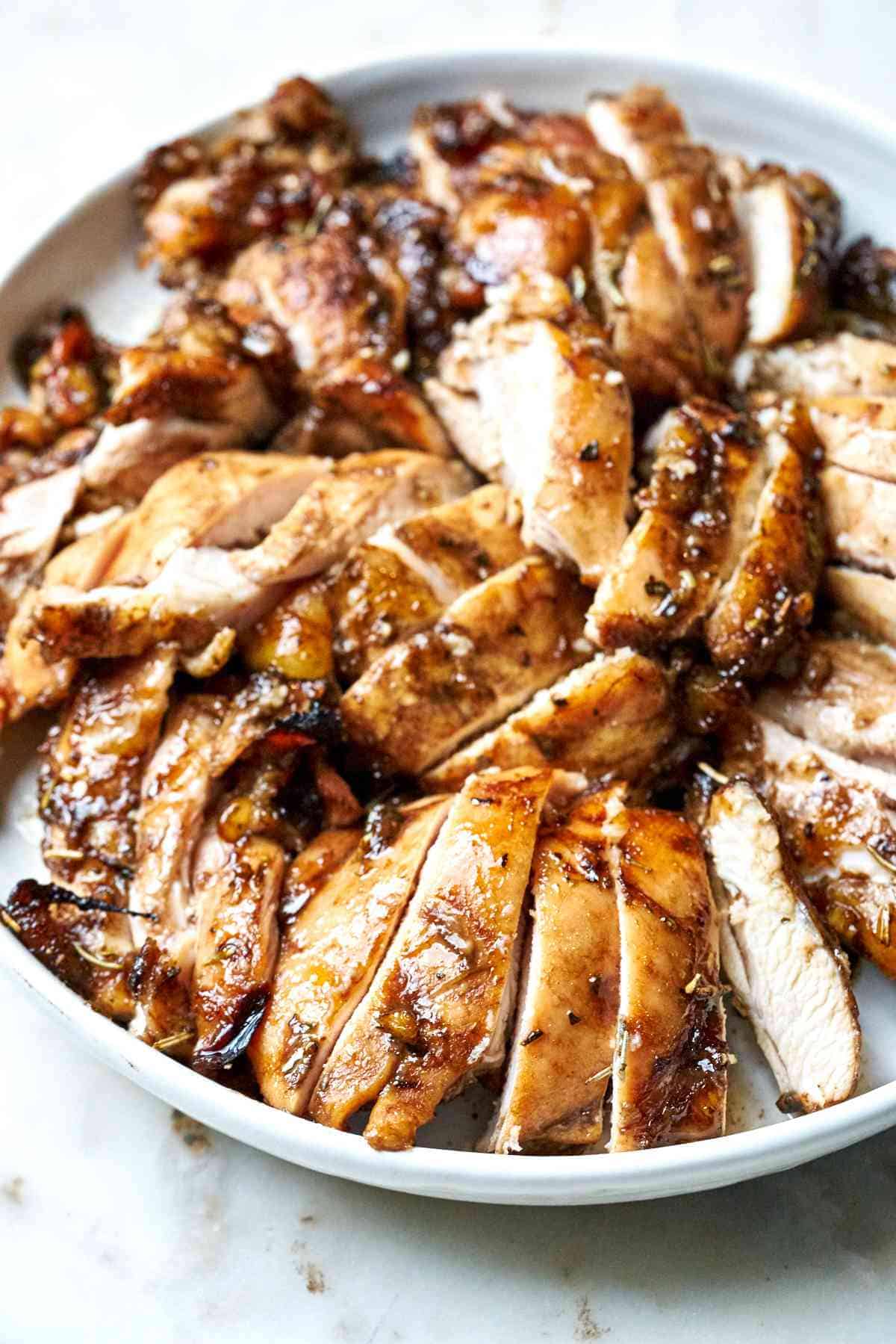 Top view of sliced chicken thighs on a big white plate.