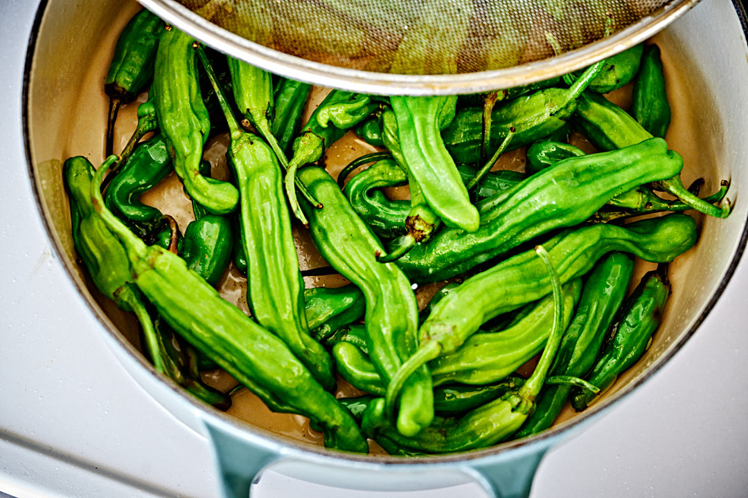 Shishito peppers simmering in a large pot on the stove.