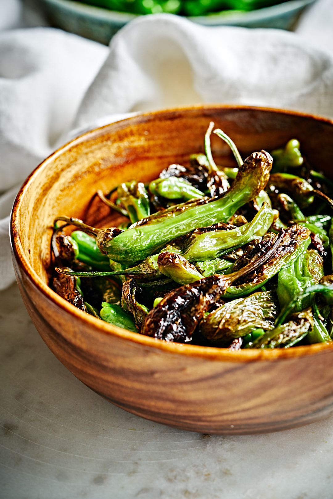 Charred shishito peppers in a large wooden serving bowl.