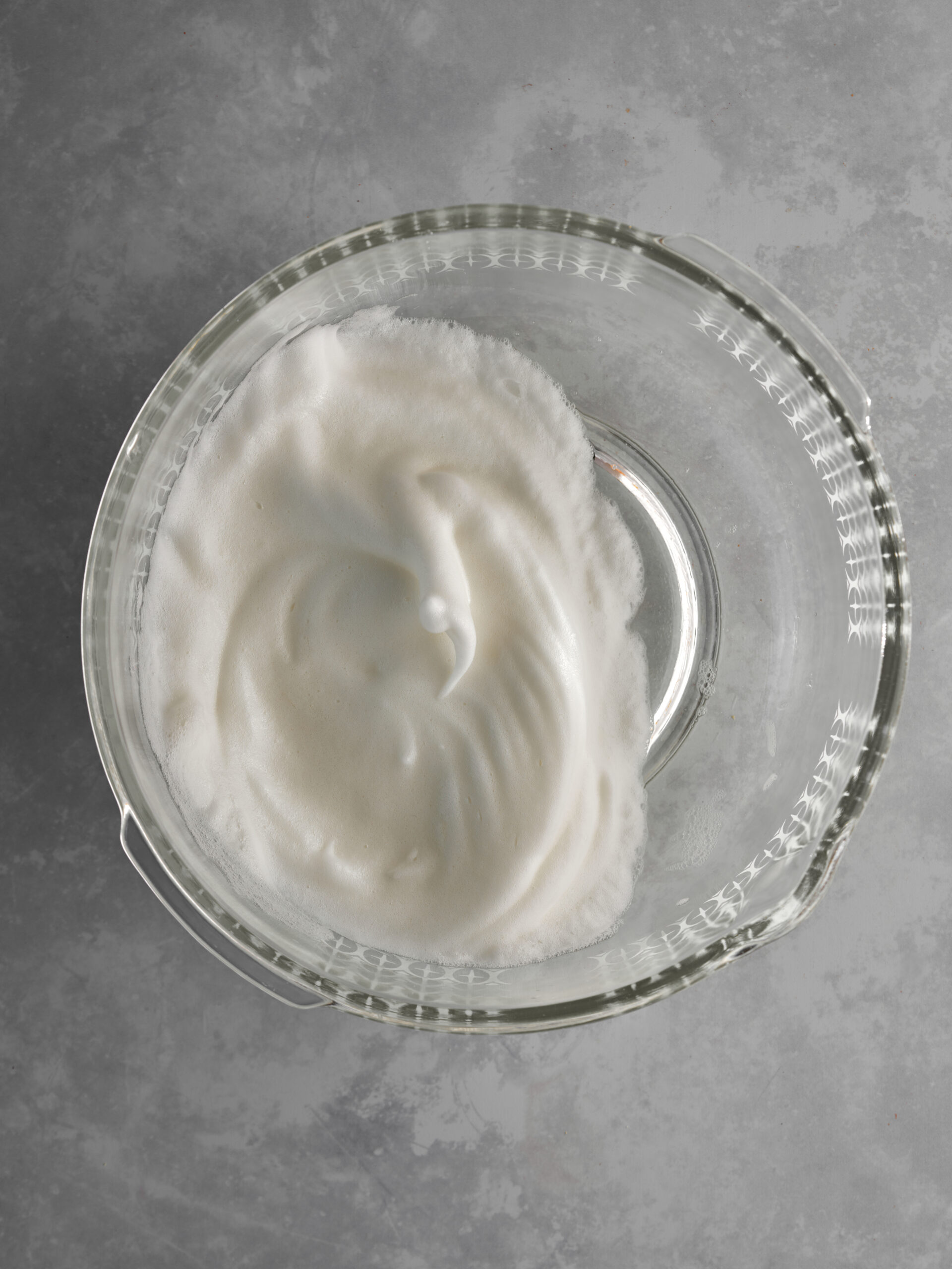 Whipped egg whites in a large glass bowl.