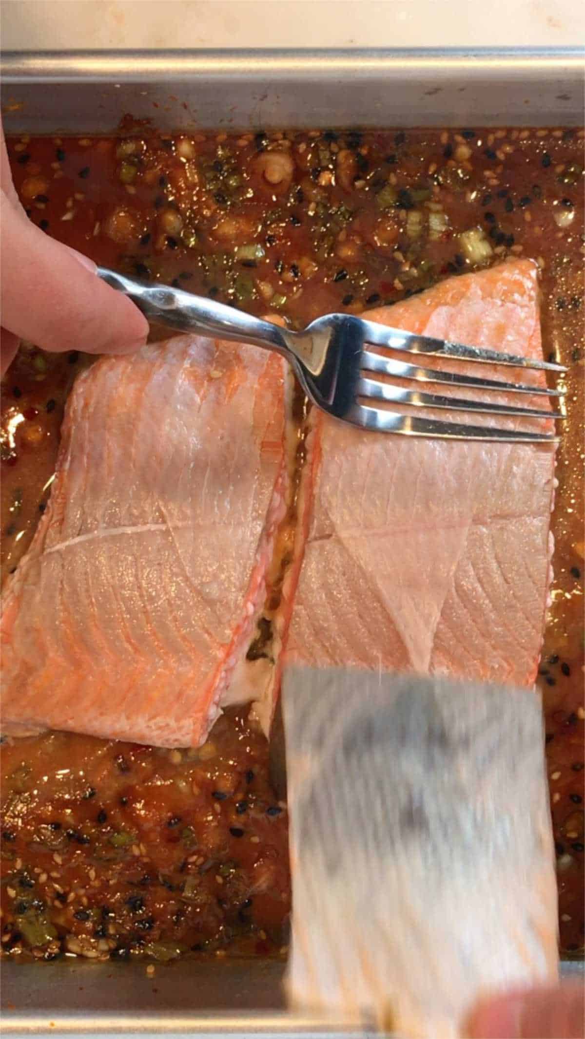 Hand using a fork to peel the skin off a salmon filet.