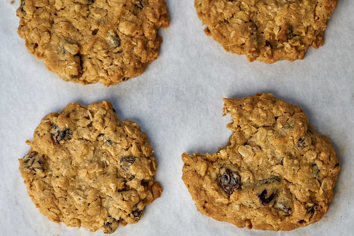 Four oatmeal raisin cookies on parchment paper with a bite taken out of one.