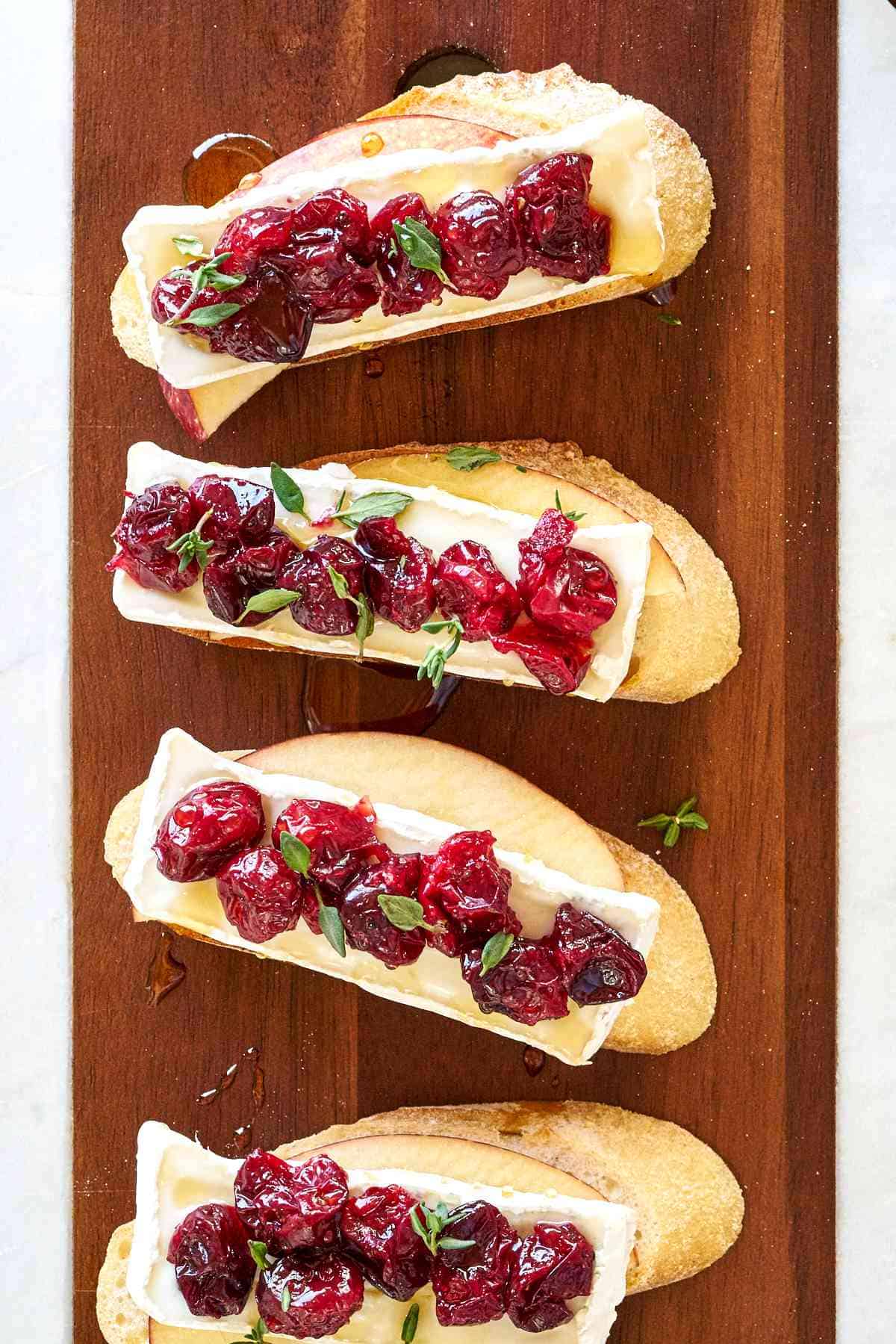 Four crostini with brie and cranberries arranged on a cutting board.