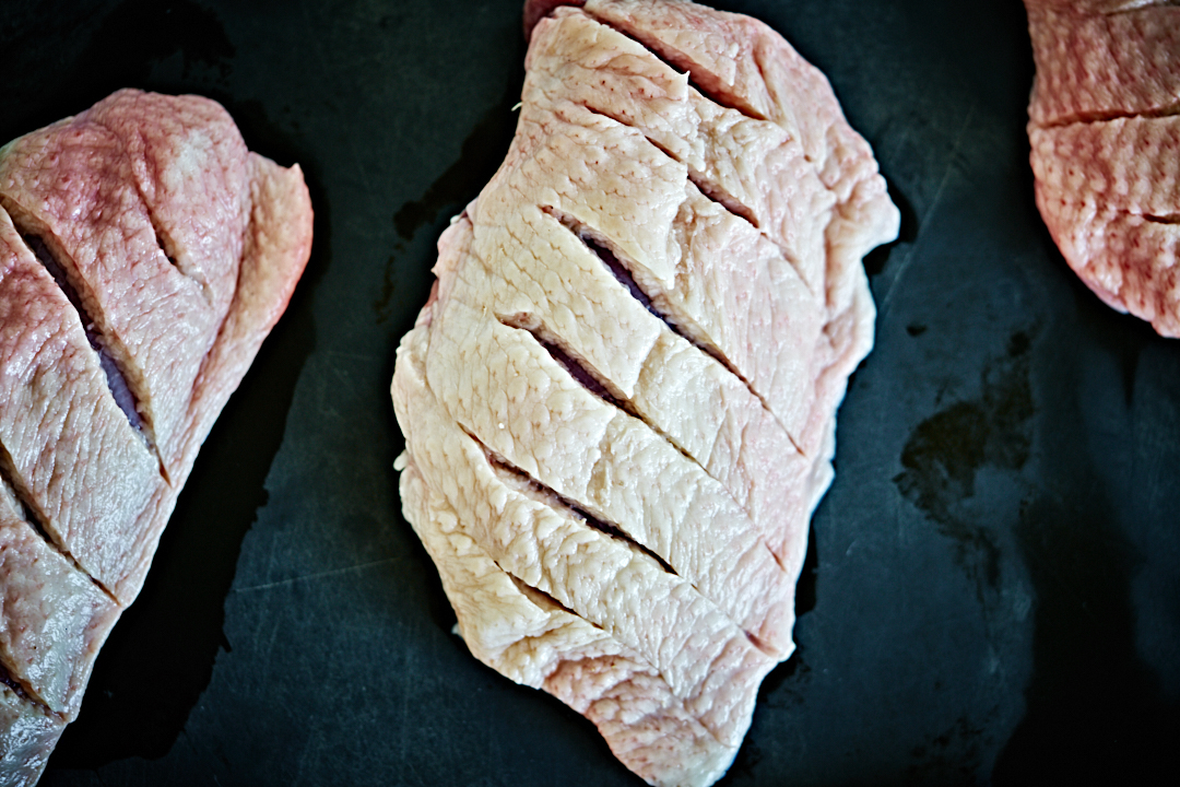 Three duck breasts on a black cutting board with scored skin.