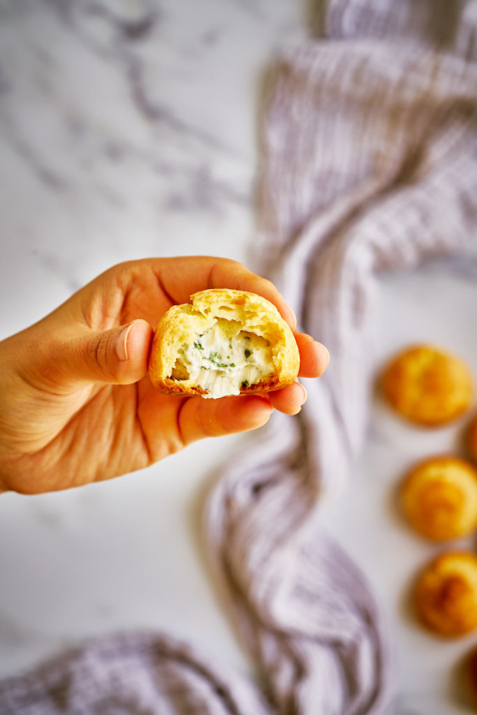 Mano che tengono il bignè ripieno di formaggio.