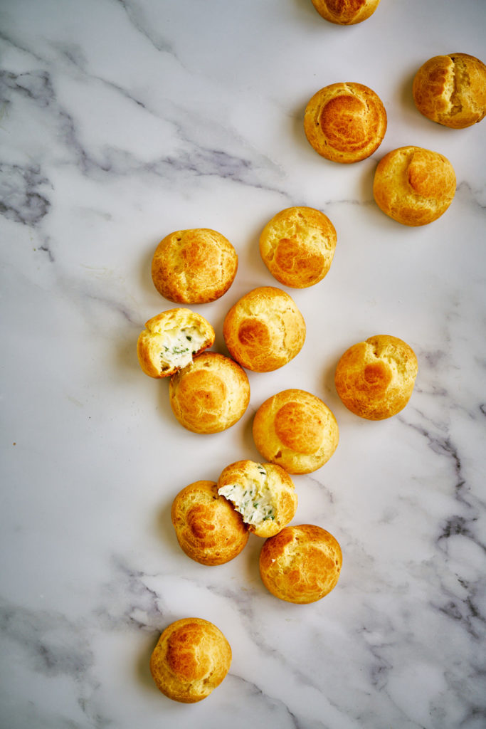 Pega de profiteroles recheados de queijo em uma superfície de mármore.