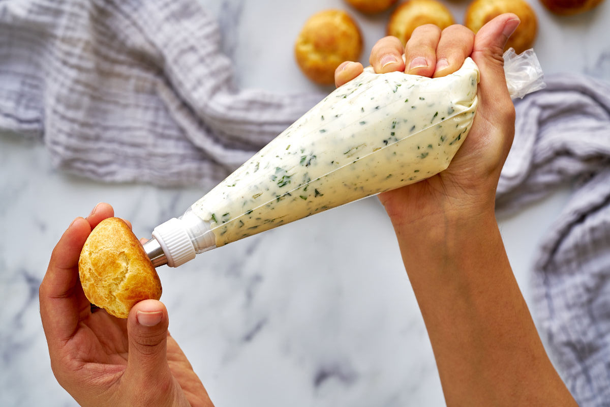 A hand holding a piping bag of cream filling and using it to push filling into a profiterole. 