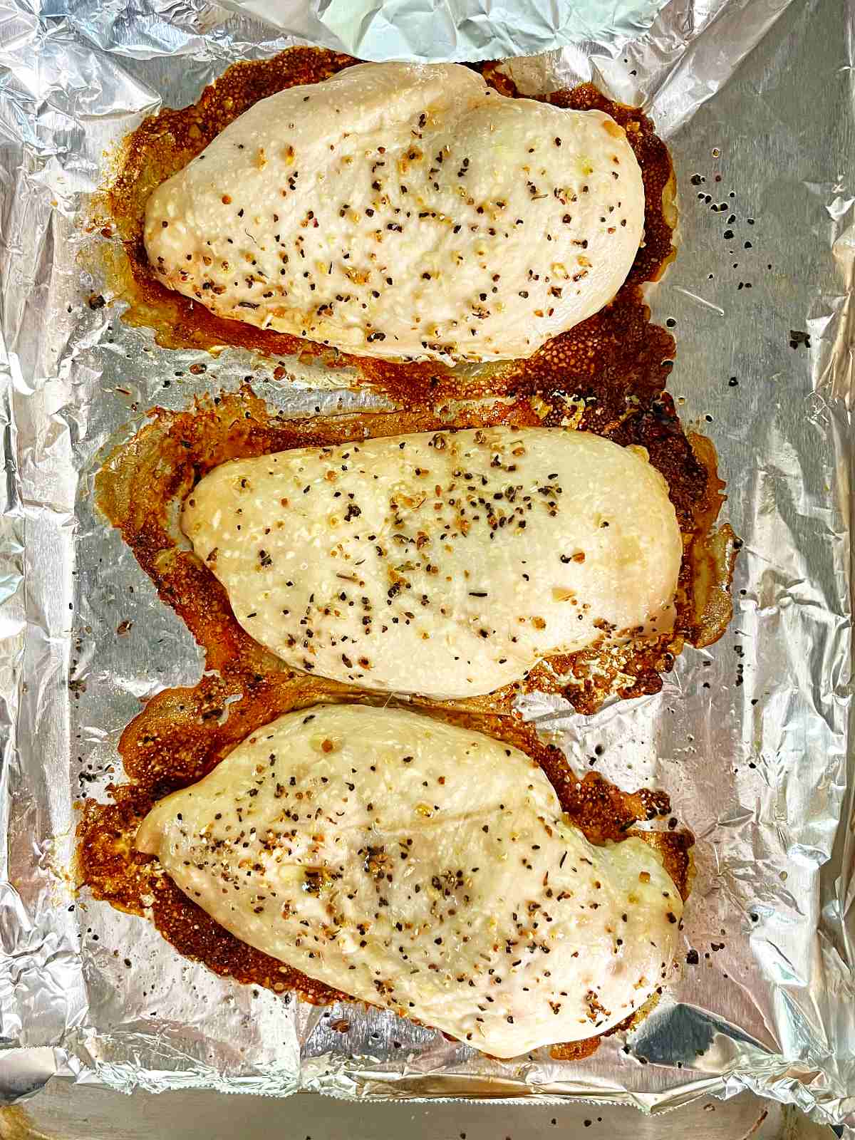 Three cooked chicken breasts on a sheet of aluminum foil.