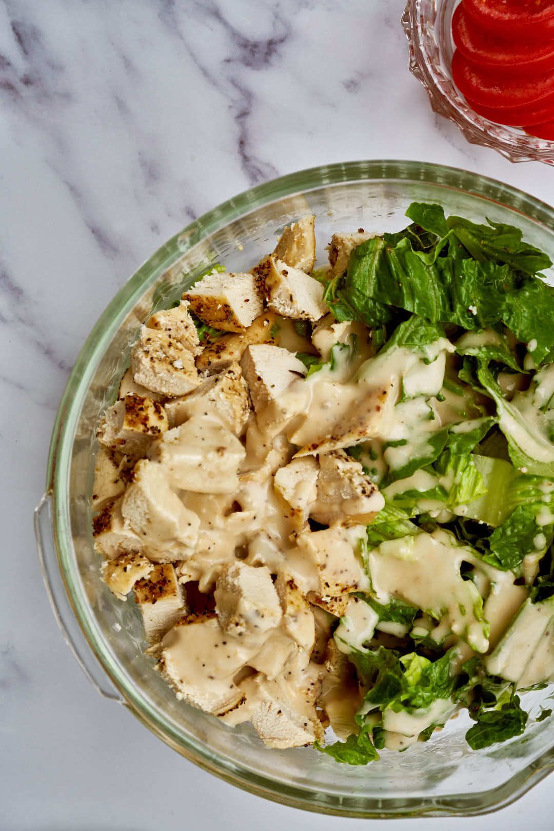 Diced chicken, lettuce, and beige dressing in a large glass bowl.