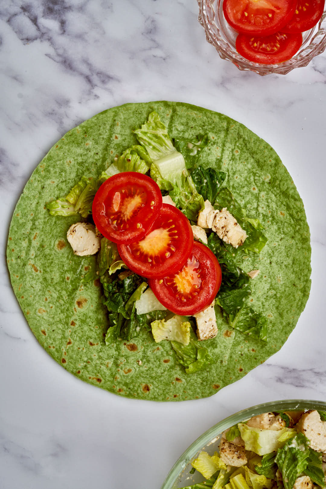 Red tomato, diced chicken, lettuce, and dressing on top of a green wrap.