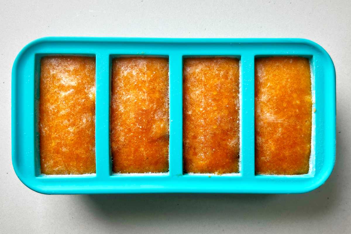 Silicone freezer cubes with orange puree on a countertop.