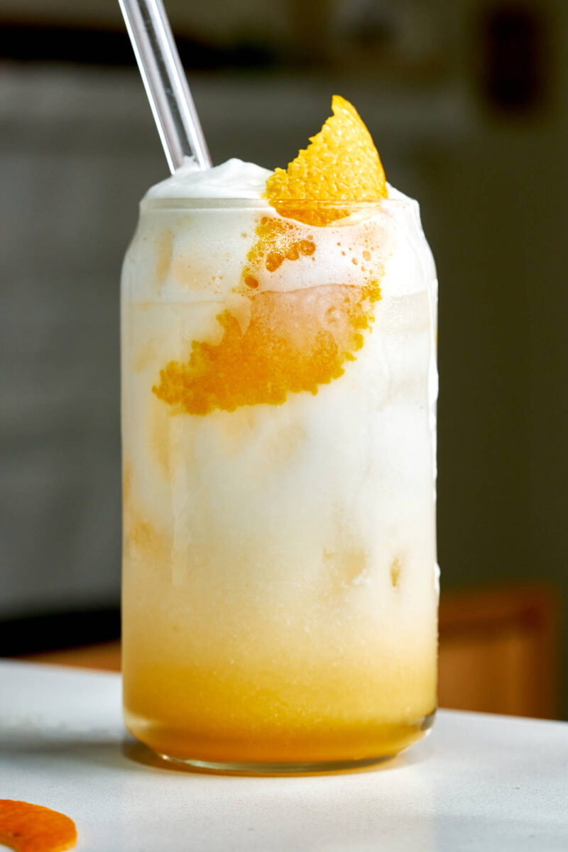Orange creamsicle in a beer can glass with a glass straw and orange rind.