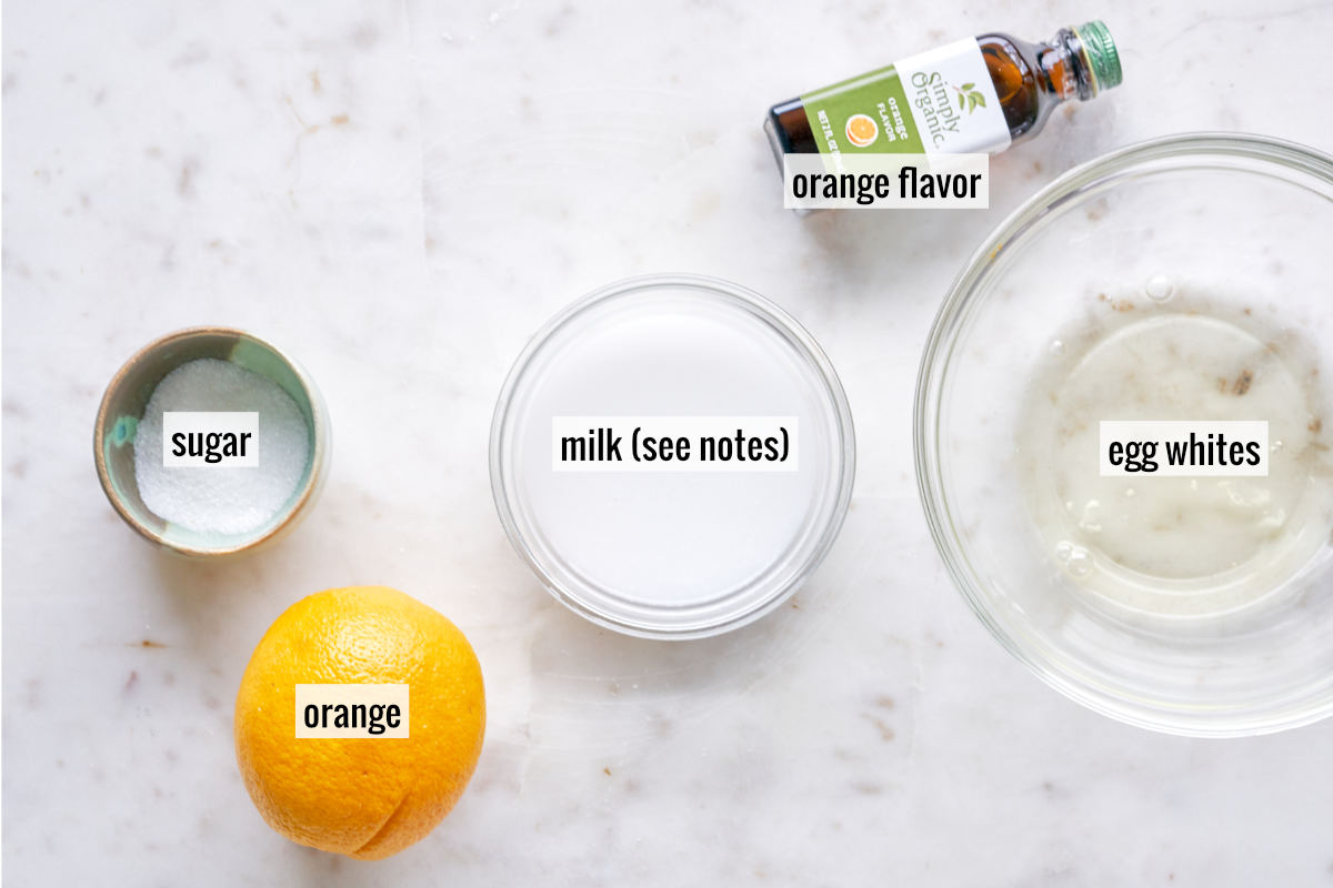 AN orange, milk, orange flavor, egg whites, and sugar on a countertop.