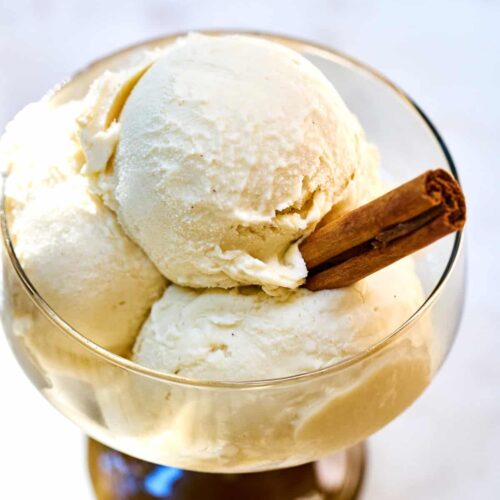 Three scoops of ice cream in a pedestal glass with a stick of cinnamon.