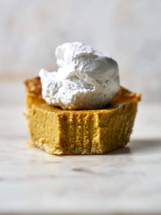 Front view of a slice of pumpkin pie with whipped cream on top.