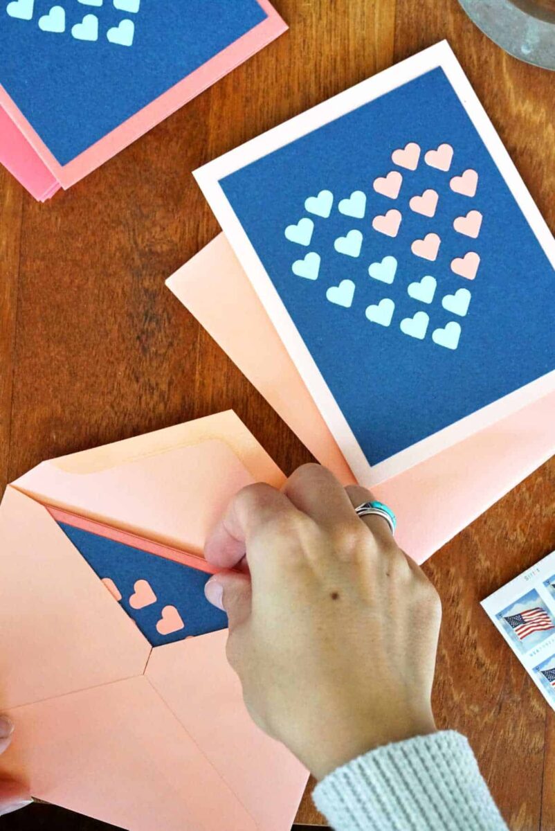 Two hands putting blue cards with hearts into pink envelopes.