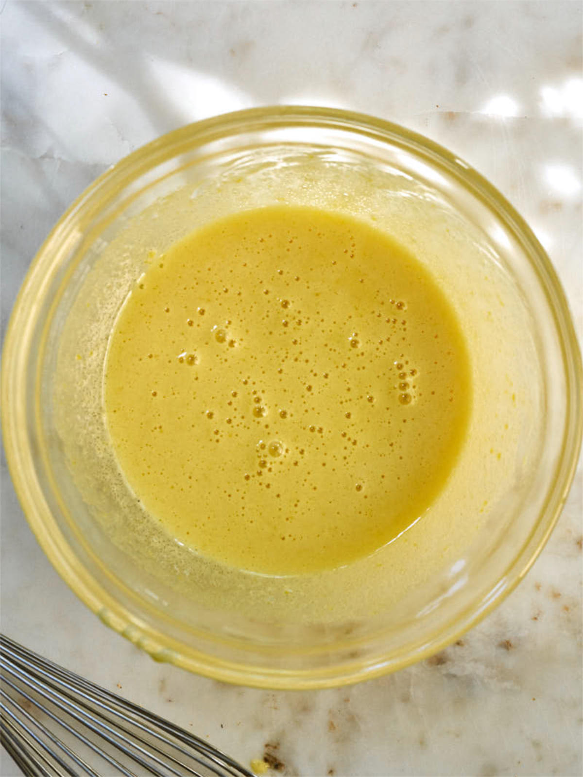 Yellow frothy liquid in a clear glass bowl next to a whisk.