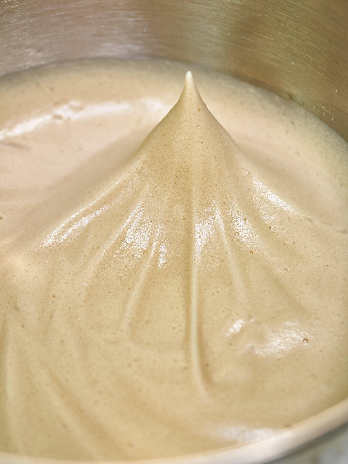 Whipped light brown meringue in a metal bowl.