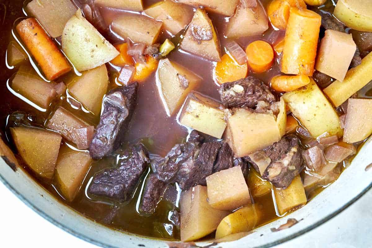 A close up of potatoes, carrots, and beef chunks in brown liquid in a large pot.