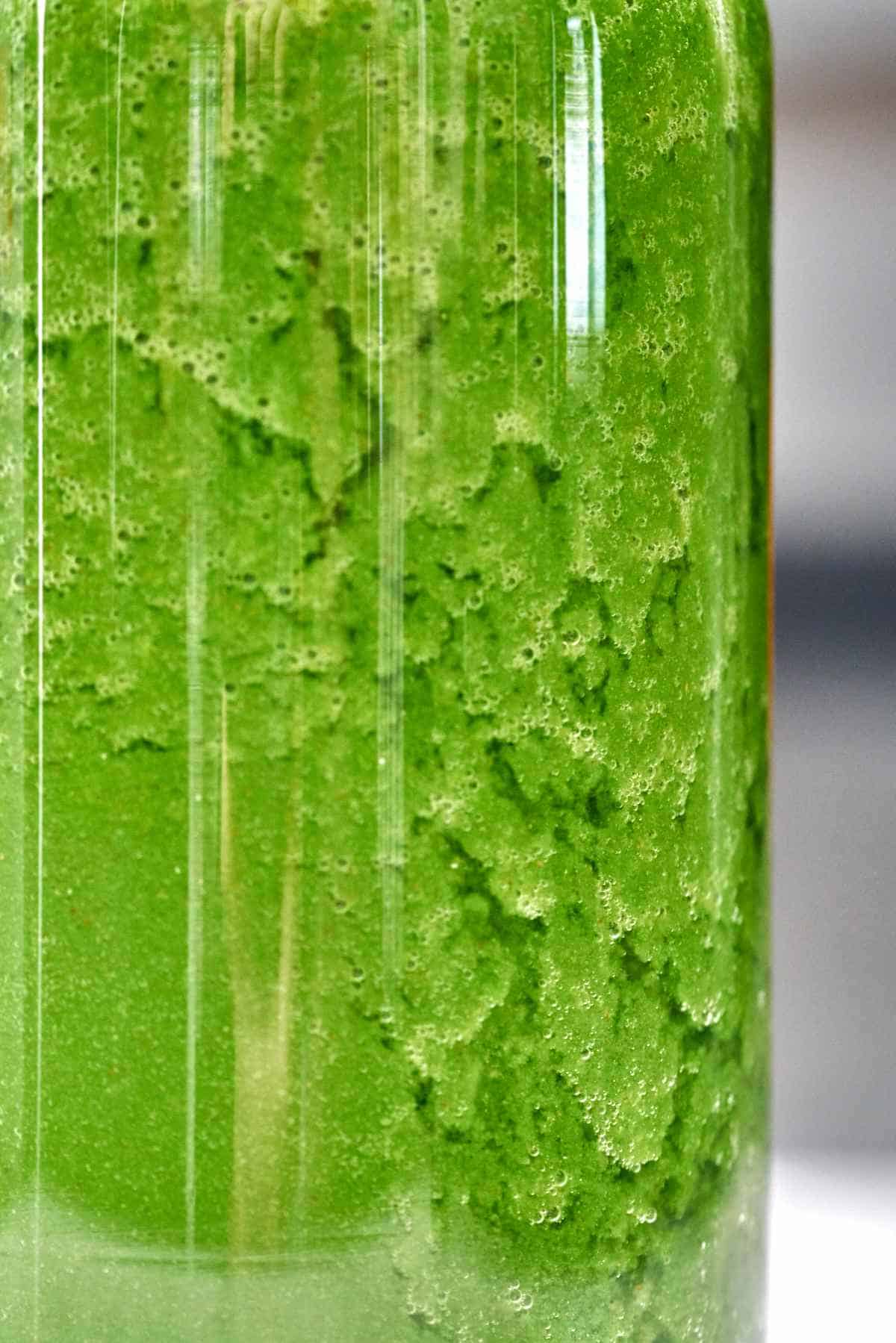 An extreme close up of green juice in a tall glass.