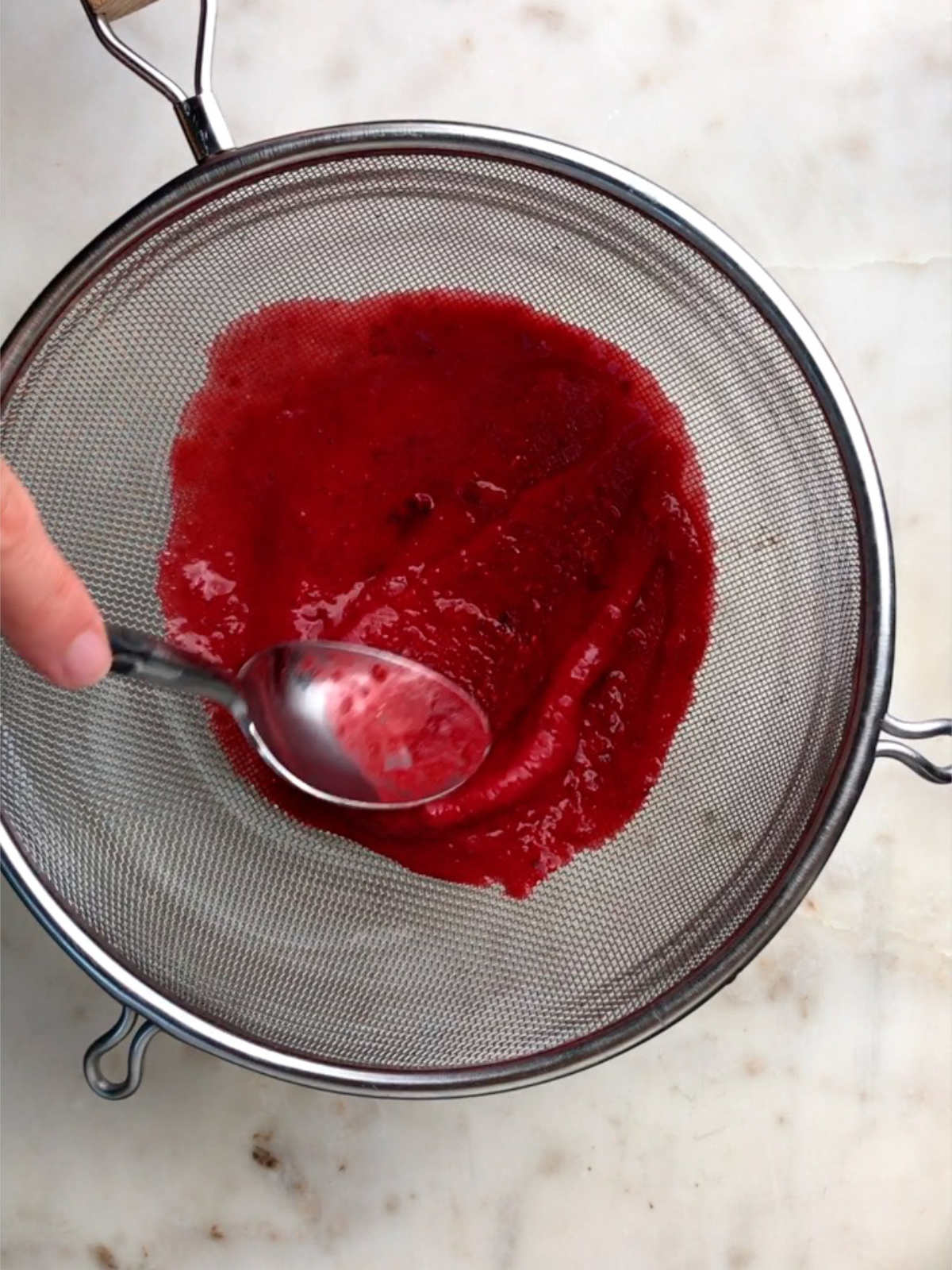 Pressing hot pink purre through a strainer.