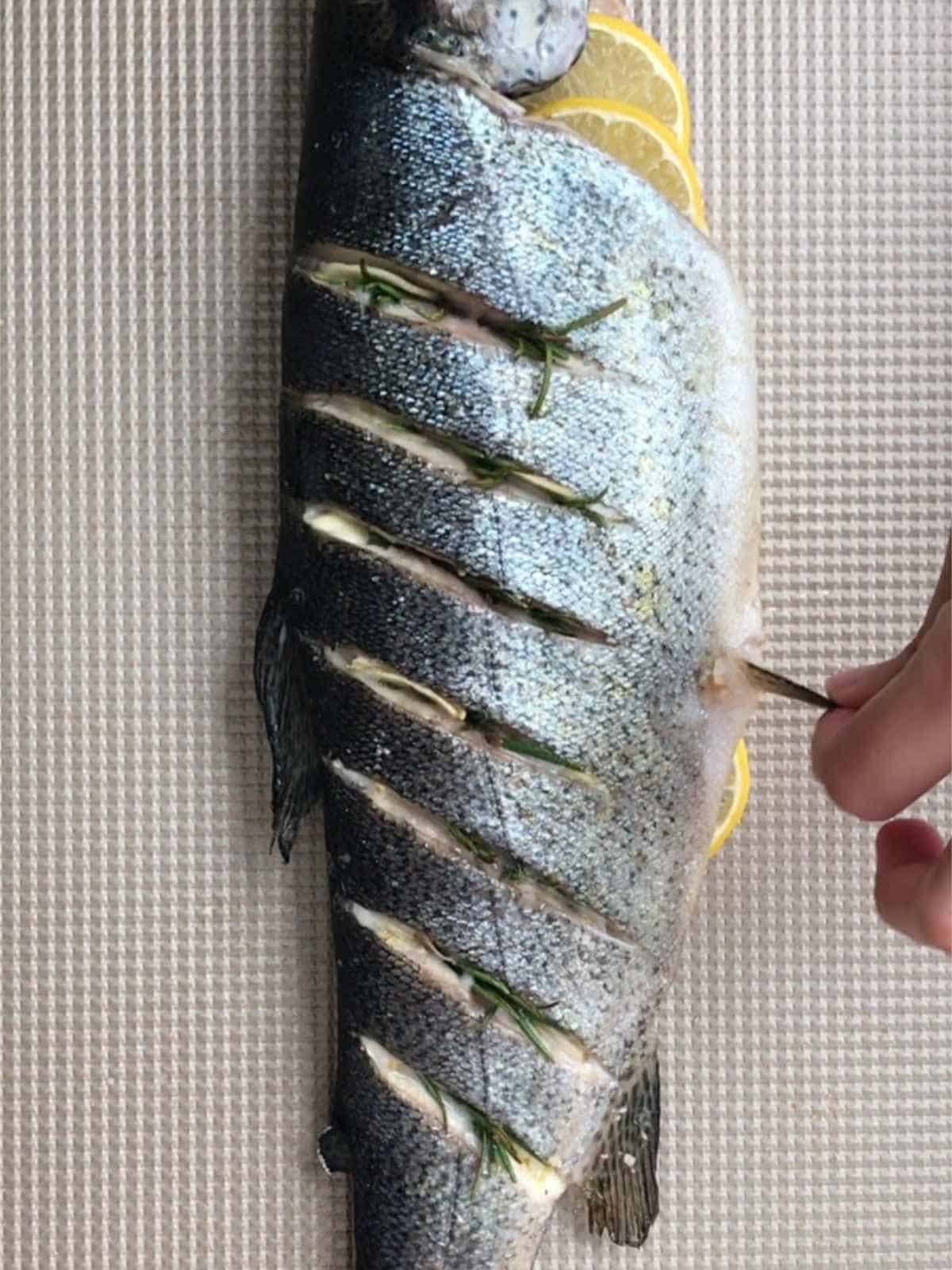 Hand tugging at a fin on a cooked trout.
