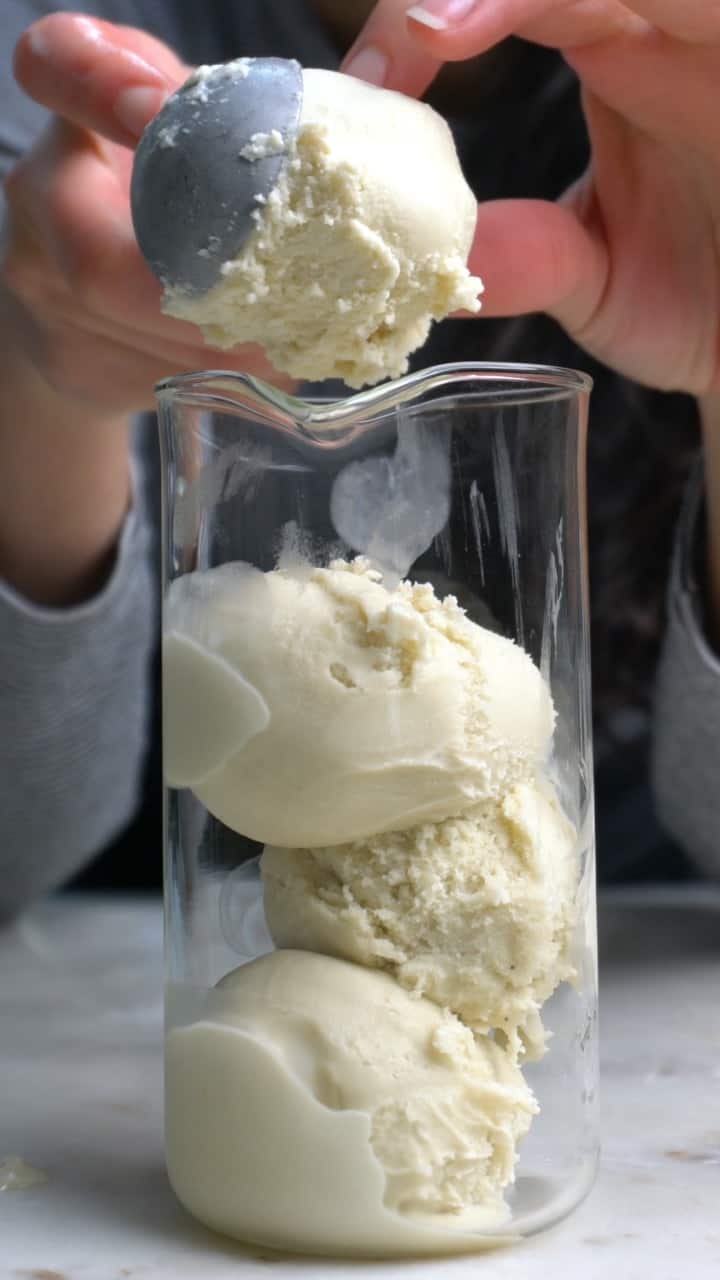 Hands using an ice cream scoop to scoop white ice cream into a glass.