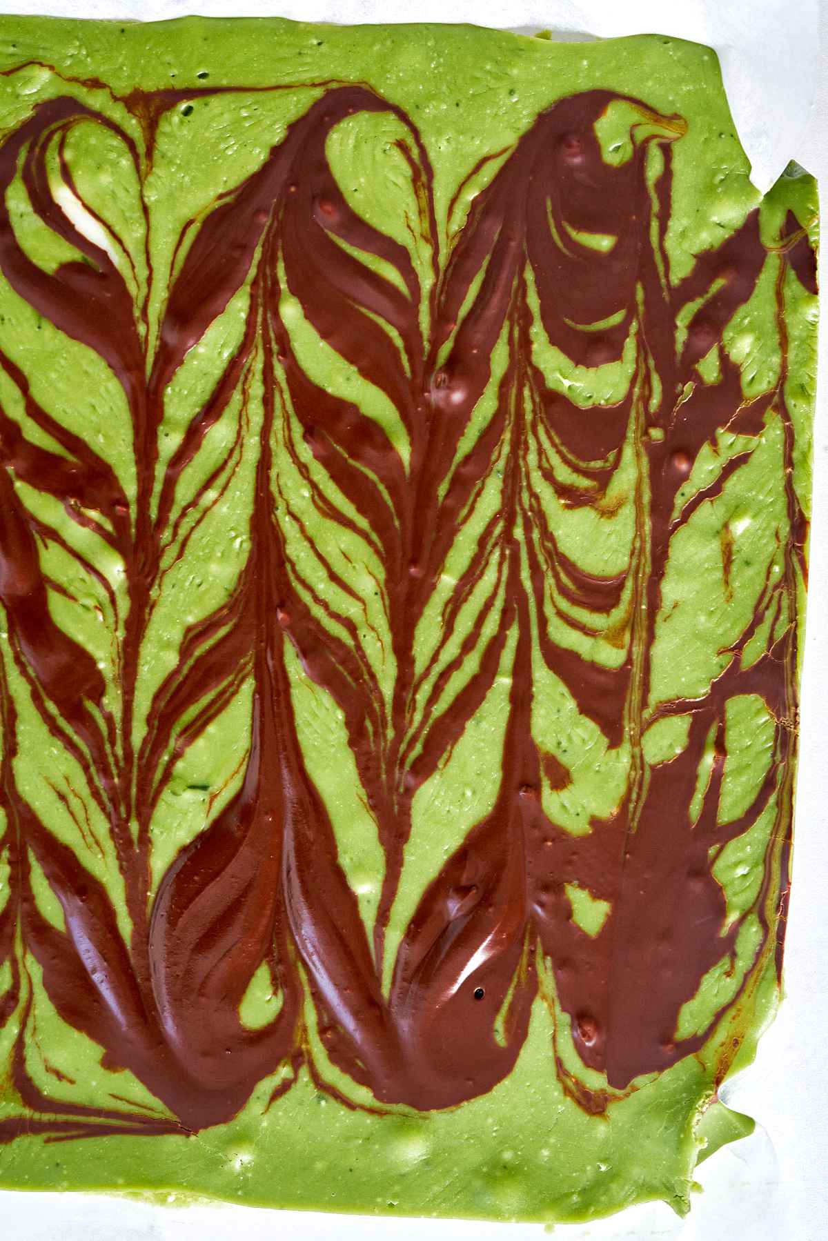 A large slab of green chocolate with a dark chocolate design.