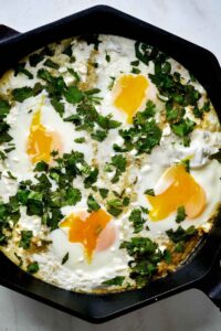 Eggs in a cast iron pan with green tomato sauce and cilantro.