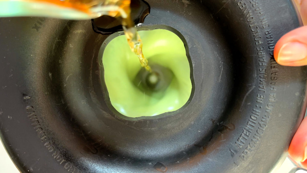 Pouring brown liquid into a blender with green liquid through the top hole.