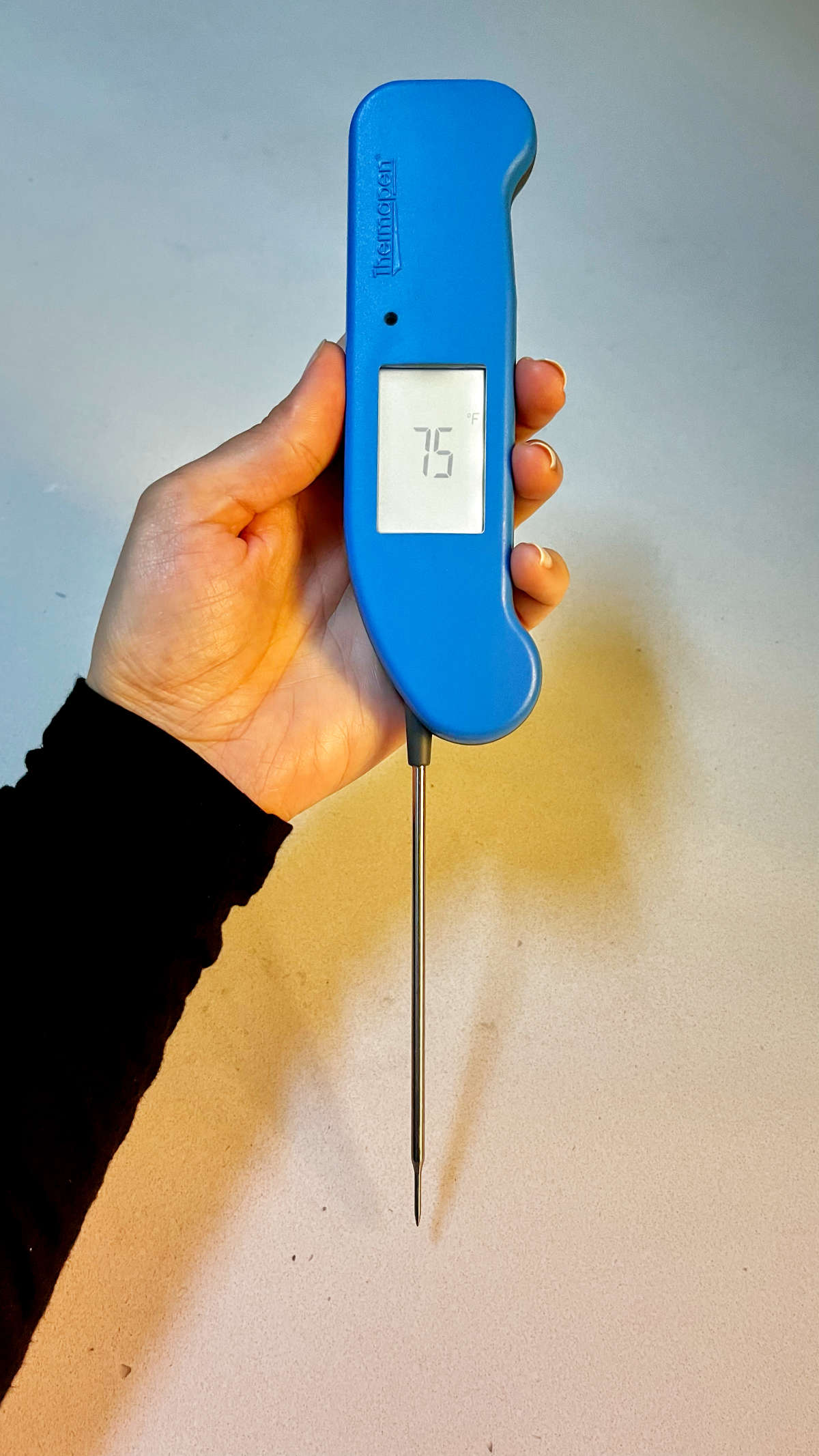 Holding a thermometer with a vertical temperature window.