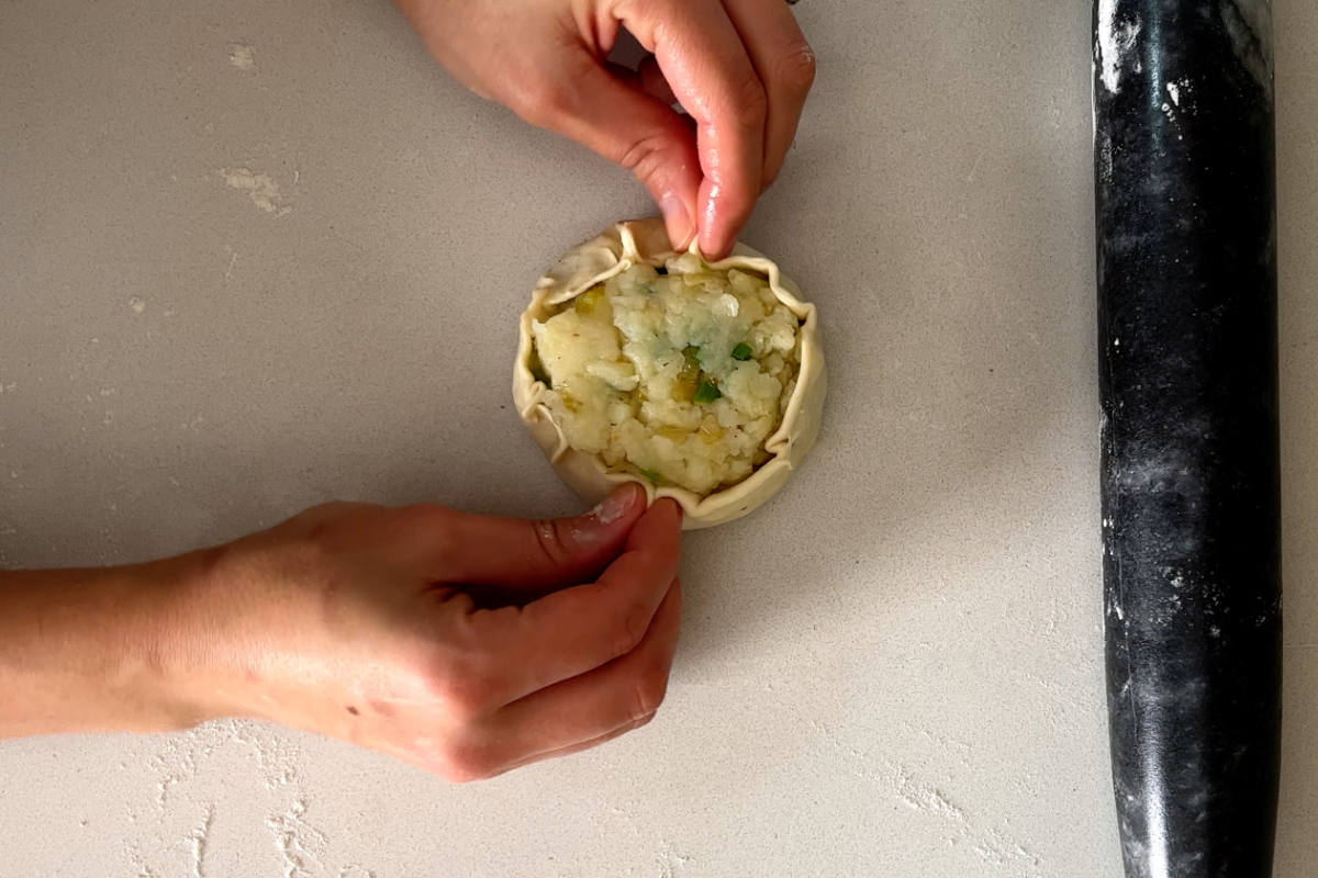 Hands pinching dough around a potato filling.
