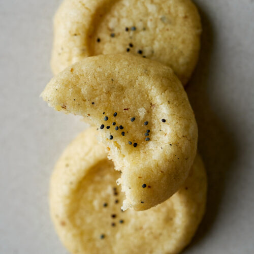 Three cookies with poppy seeds and one with a bite taken out of it.