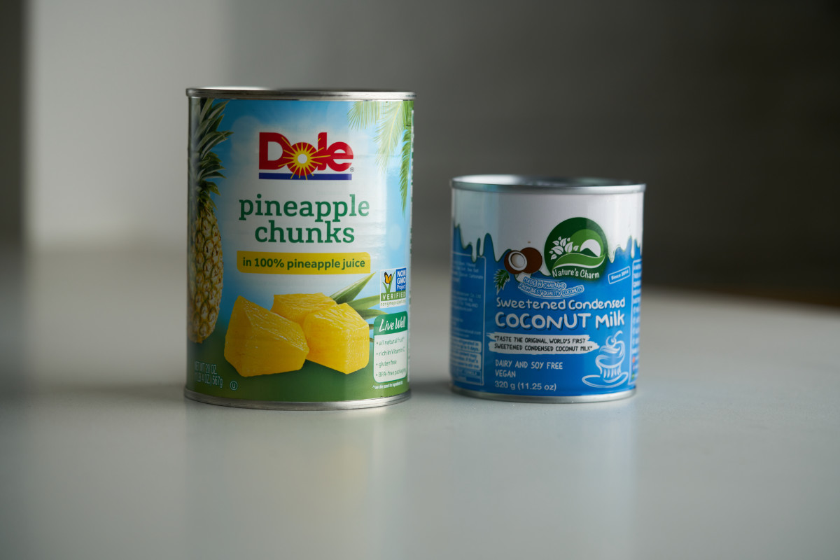 A can of pineapple chunks next to a can of sweetened condensed coconut milk.