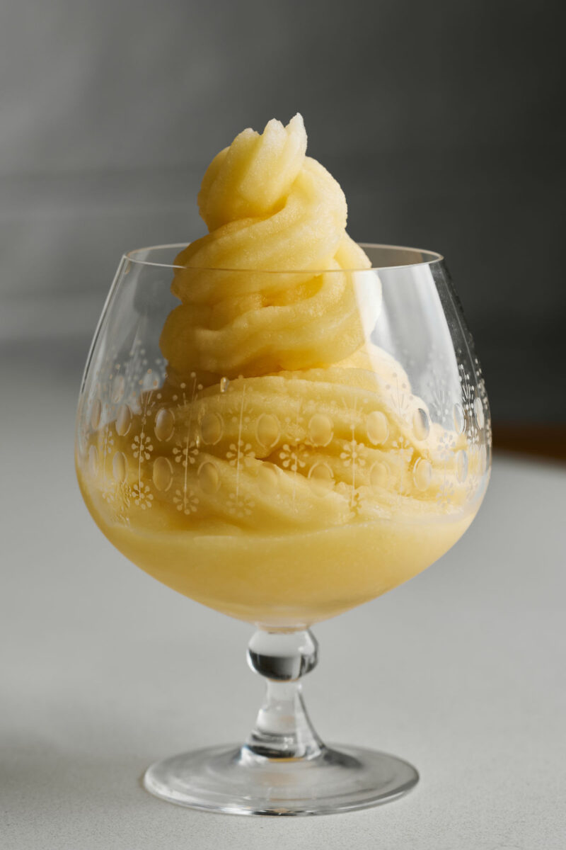 Yellow soft serve in a cognac pedestal glass.