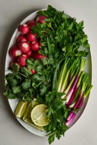 Top view of a plate filled with herbs, scallions, limes, and radishes.