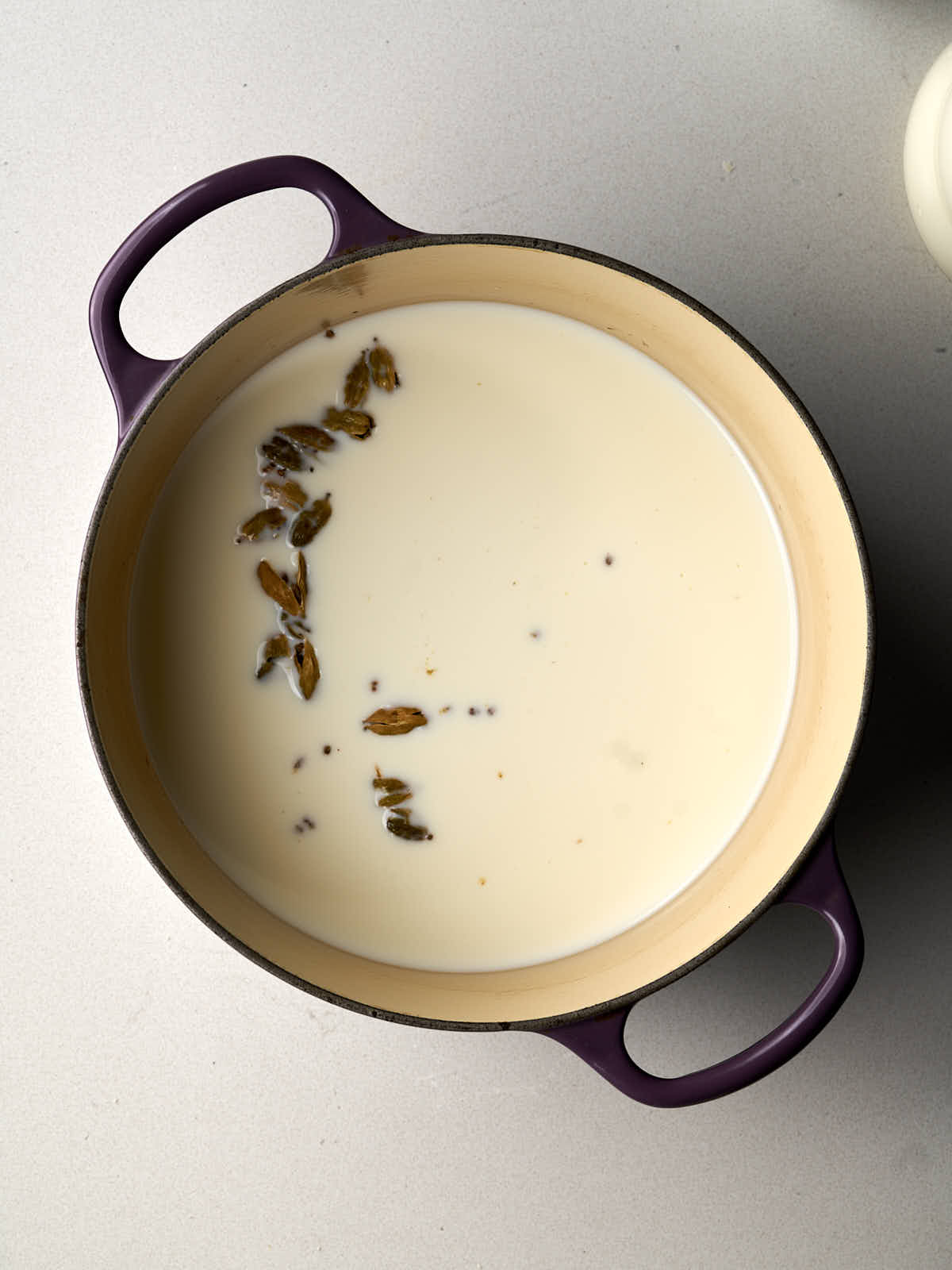 Spiced milk in a cast iron pot with a white rubber spatula.