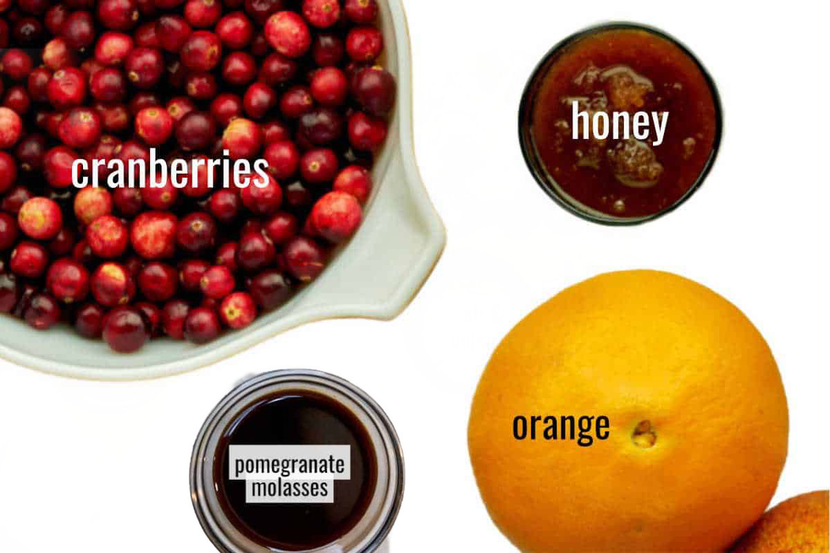 Cranberries, an orange, honey and pomegranate molasses on a white background.