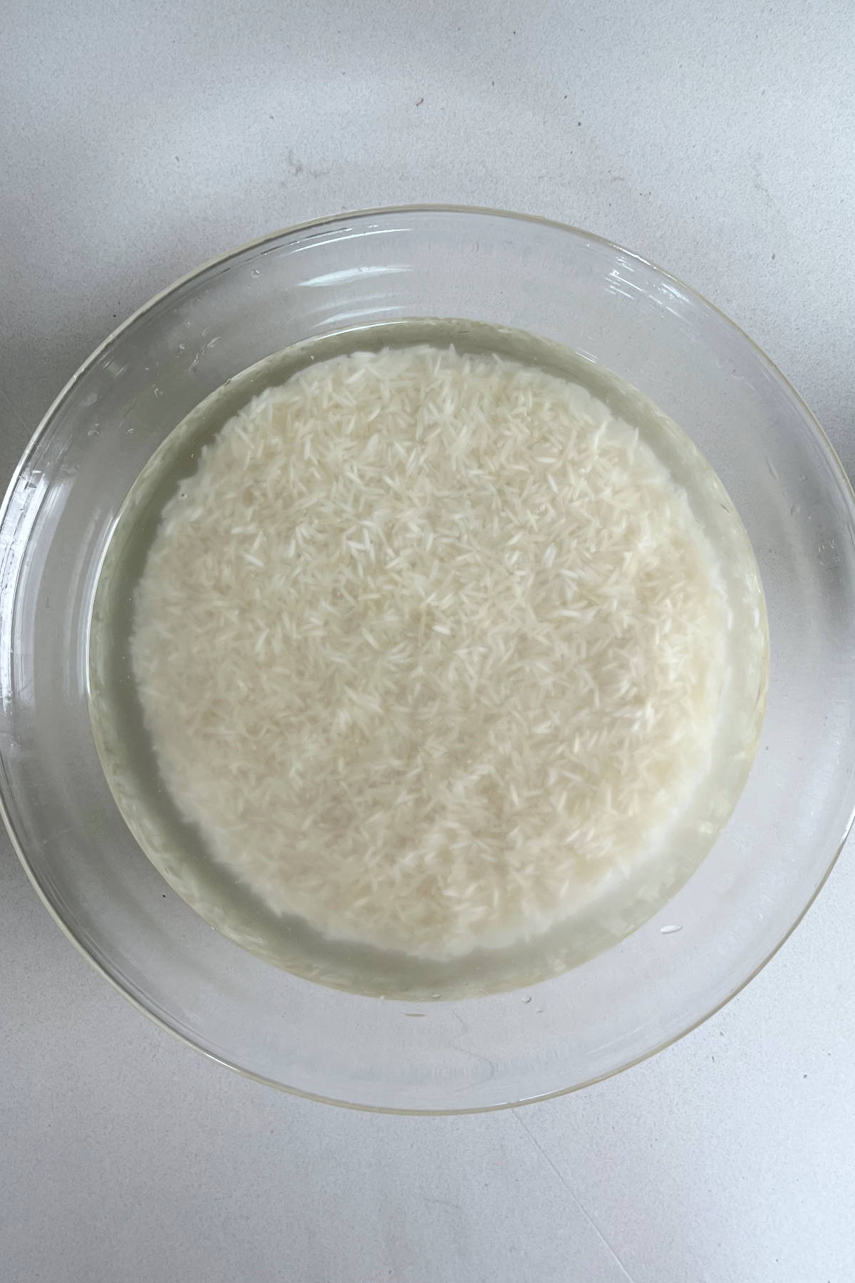 White rice soaking in a clear bowl filled with water.