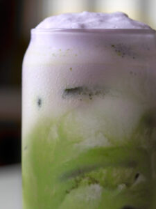 Close up of a matcha latte in a class with purple foam on top.