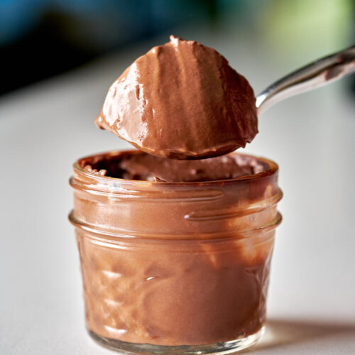 Chocolate pudding in a small glass jar with a large spoonful of pudding held over the jar.