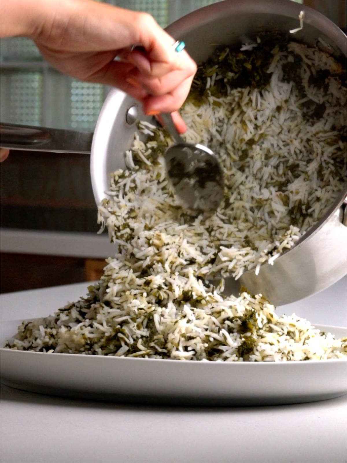 Pouring herbed rice from a metal pot into a white oval serving platter.