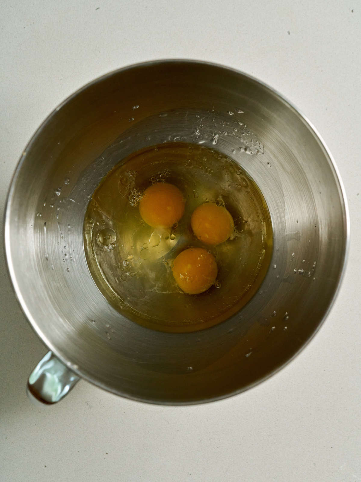 Metal stand mixer bowl with eggs and oil.