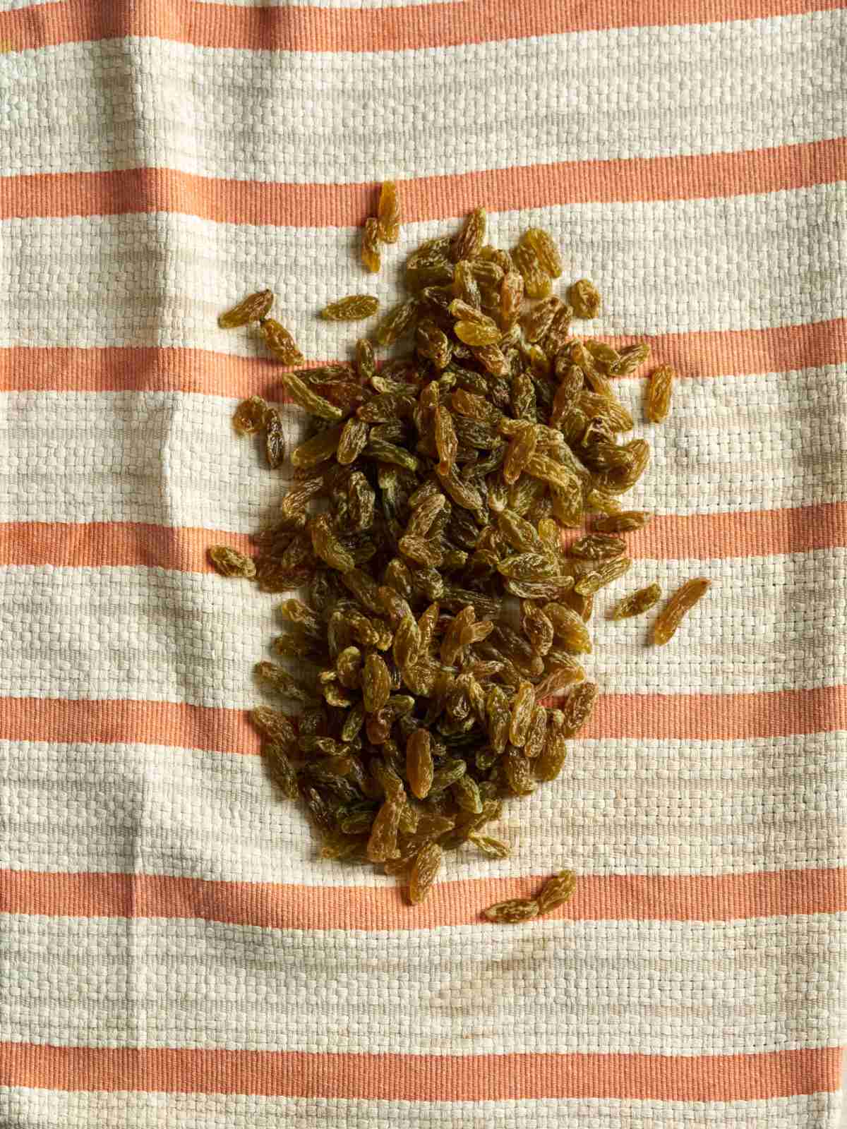 Golden raisins on a white and orange striped dish towel.