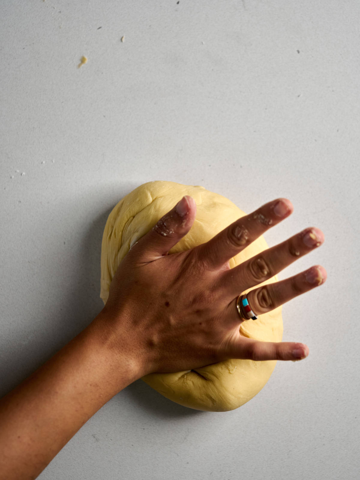 A tanned hand kneading a ball of challah dough.