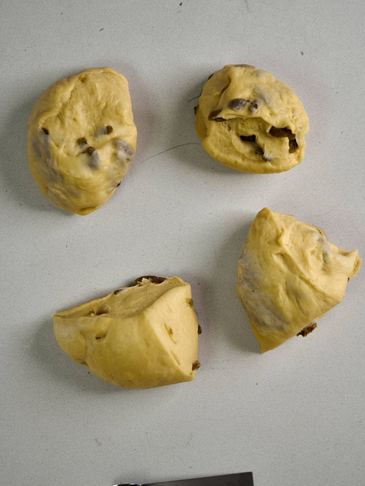 Four dough balls with raisins next to the edge of a pastry cutter.