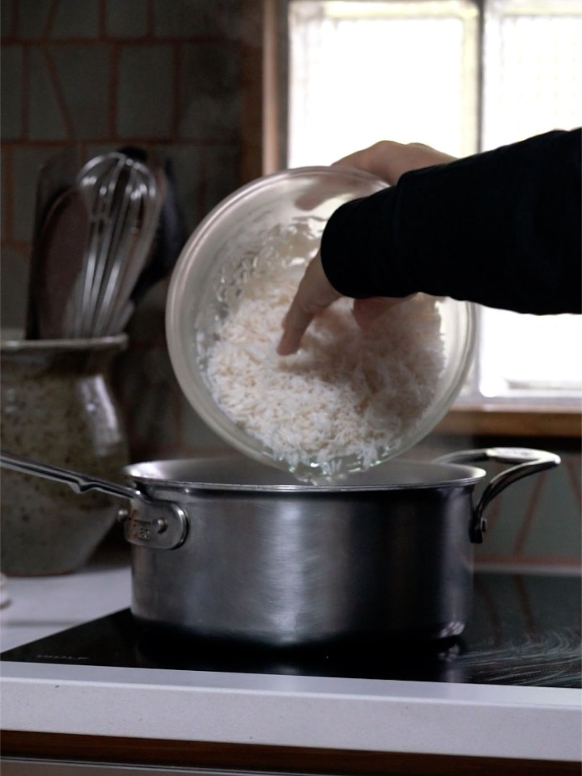 Two hands pouring rice into a metal pot.