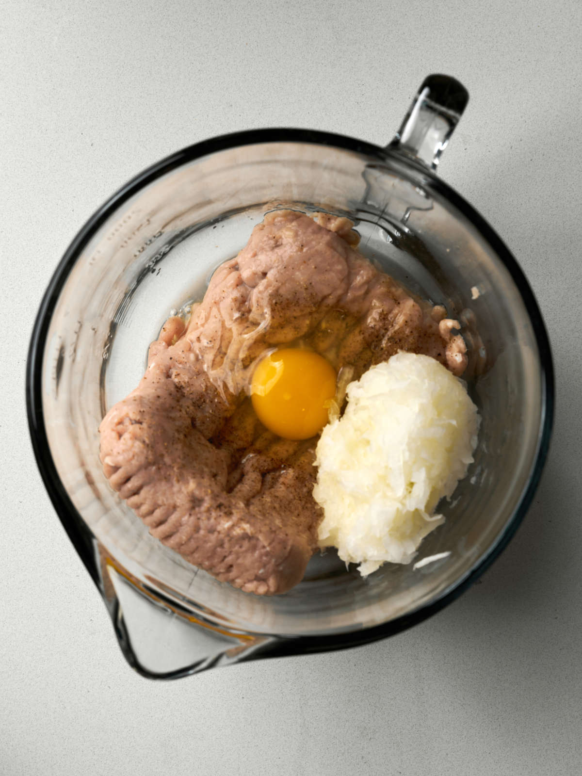 Ground chicken, an egg yolk, and grated onion in a glass bowl.